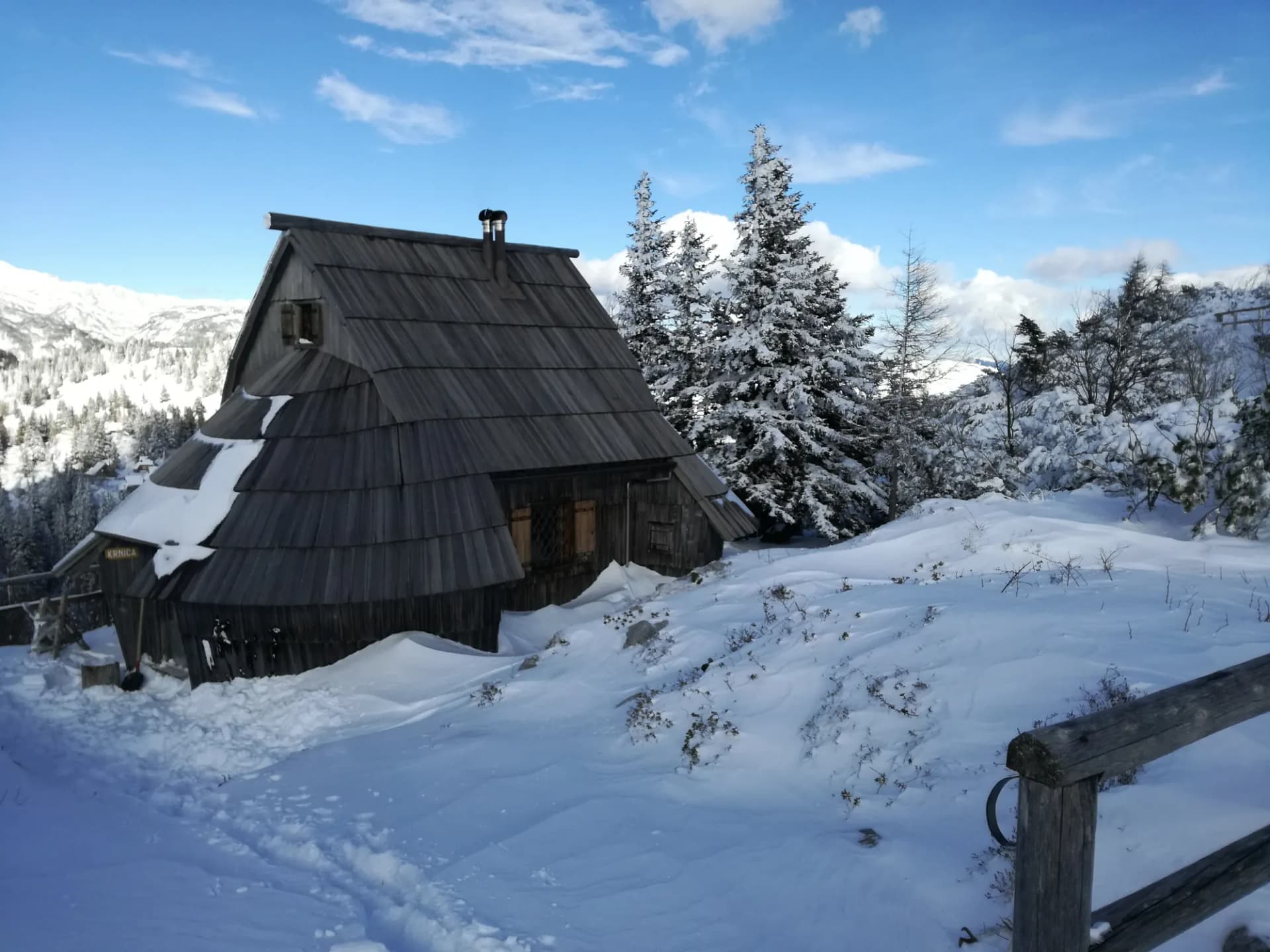 Koča Krnica pozimi, lesena bajta s skodlasto streho med zasneženimi smrekami