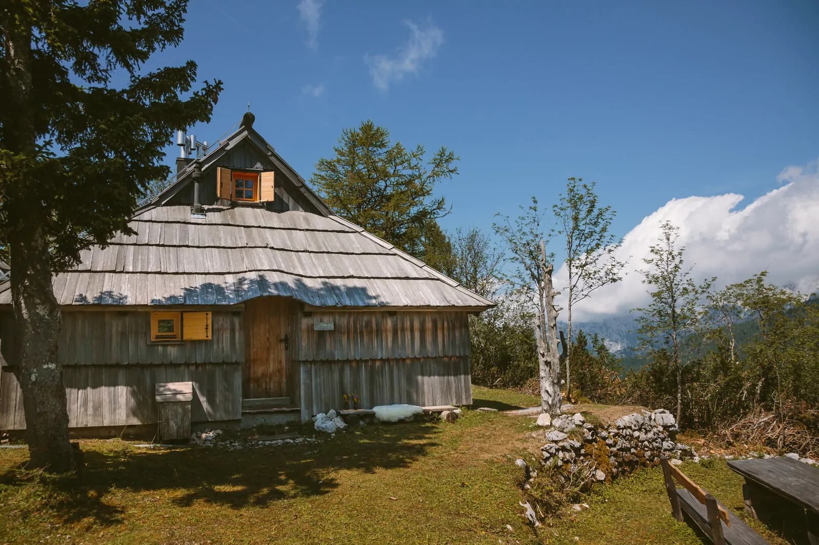 Koča Orlica na travniku Velike planine z odprtim razgledom na doline in modro nebo